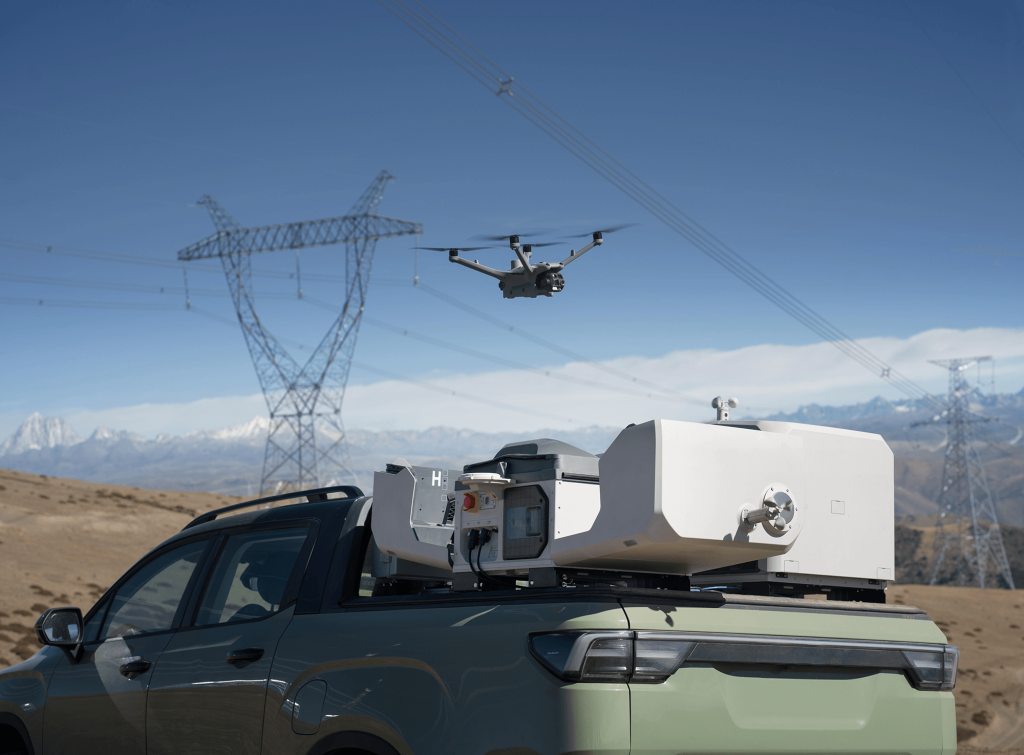 Dron de inspección aérea desplegado desde una estación móvil junto a torres de transmisión eléctrica.