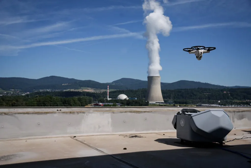 Estación Hive en azotea de instalación industrial con dron en vuelo de inspección junto a torre de enfriamiento.