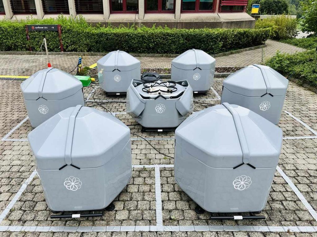 Flota de estaciones Hive dispuestas en patio exterior junto a un dron desplegado en el centro.